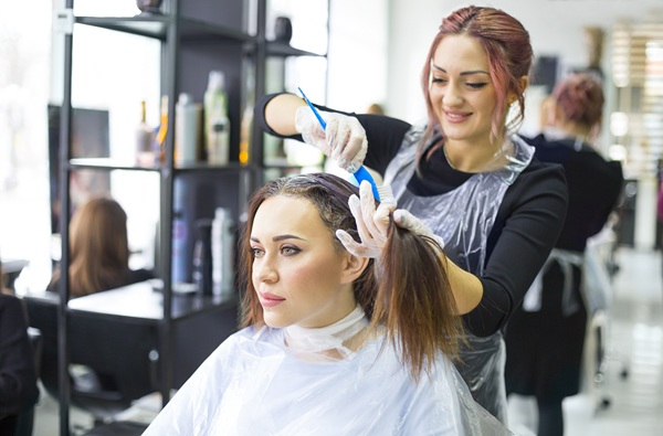 Professional female hairdresser applying color to female customer at design hair salon, woman having her hair dyed. Hair dye colouring in process
